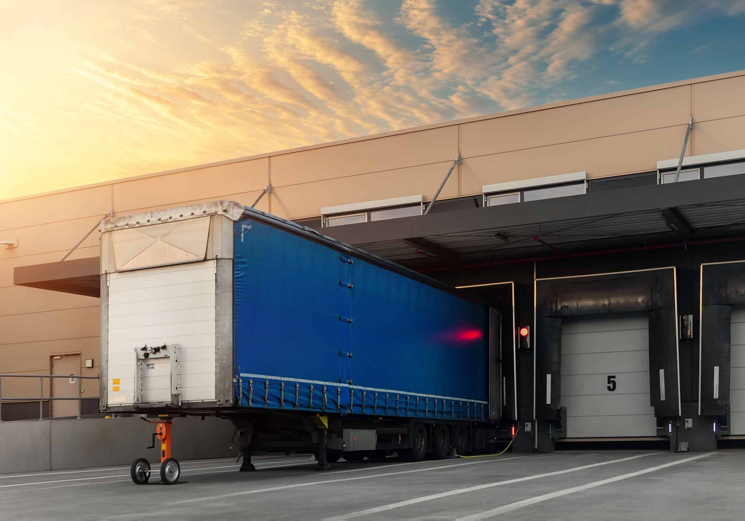 Innovative modern logistics warehouse center complex building exterior bay gate semi-trailer unloading goods distribuition warm blue sunset sky background. Cargo storage facility industry building Innovative modern logistics warehouse center complex building exterior bay gate semi-trailer unloading goods distribuition warm blue sunset sky background. Cargo storage facility industry building.